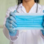 Asian woman in doctor gown or lab coat showing how to correctly wear hygiene surgical mask, demonstrating the method to save health from virus outbreak and dirty air.